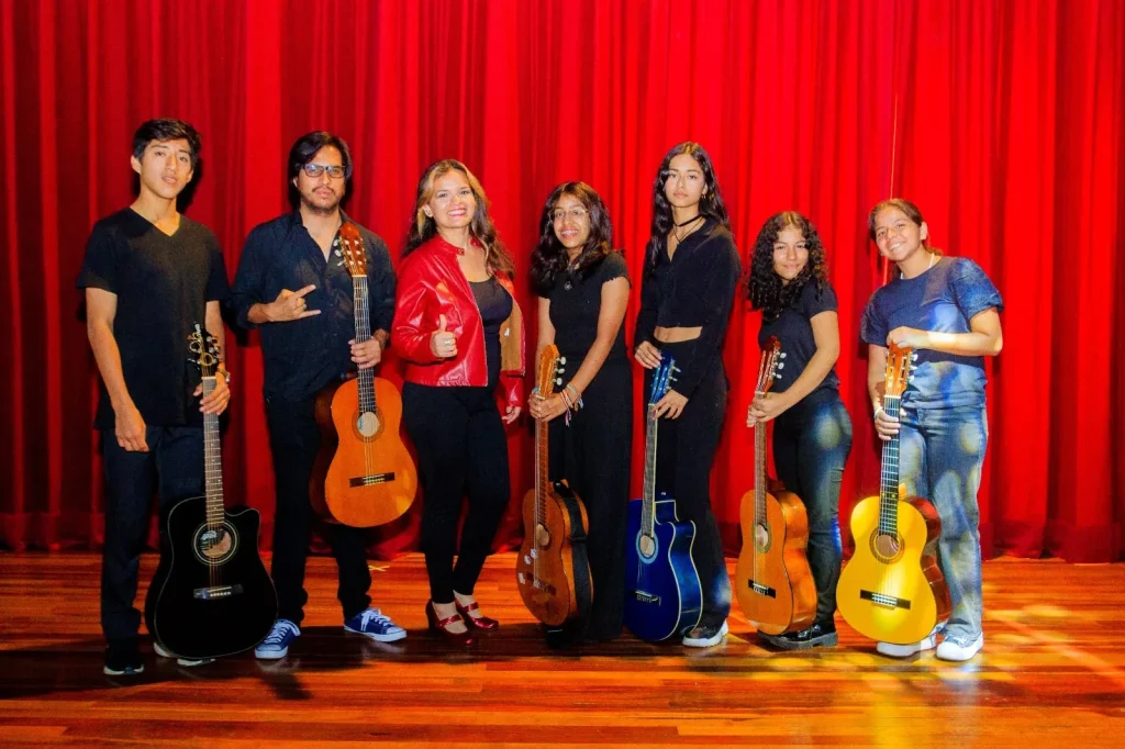 Alumnos con sus guitarras sobre un escenario con telón rojo