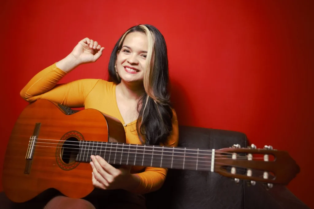 La profe Yodira sonriendo con su guitarra sobre un fondo rojo