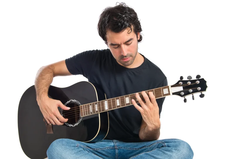 Hombre tocando una guitarra acústica sentado en el suelo
