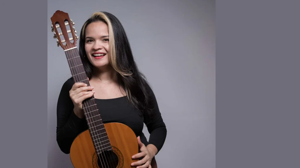 La profe Yodira con su guitarra sobre un fondo gris
