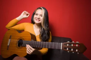 La profe Yodira sonriendo con su guitarra sobre un fondo rojo
